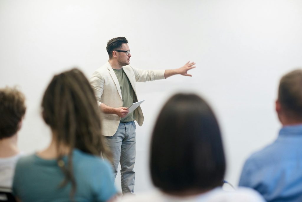 A man giving a presentation to a group of people while holding a tablet and pointing to his left. 