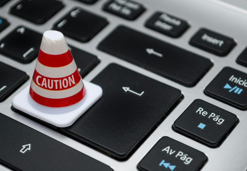 A tiny traffic cone with the word caution printed on it in all caps next to an enter button on a keyboard