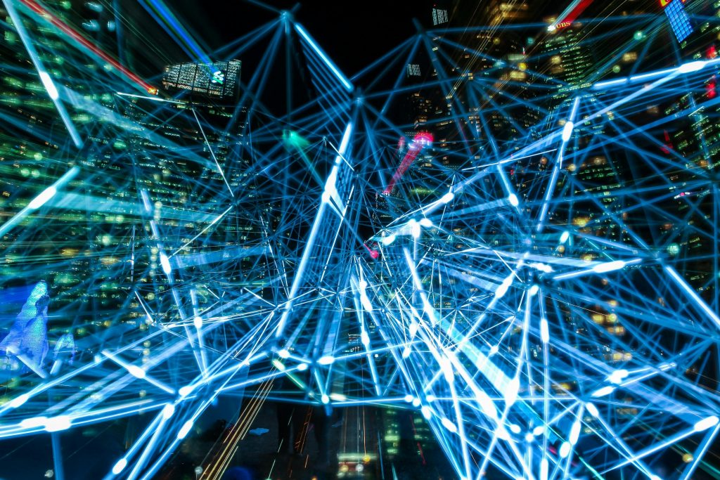 A complex network of blue lights in front of tall city buildings at night, with many lights on in the windows