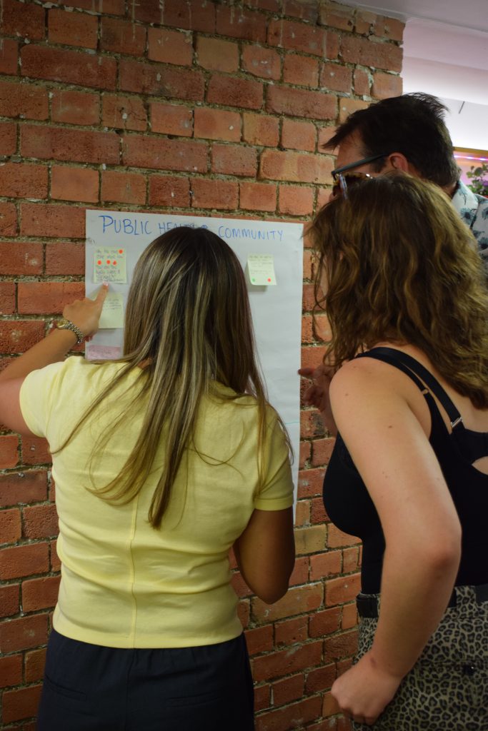 Three people looking at a poster on a wall with post-it notes stuck to it
